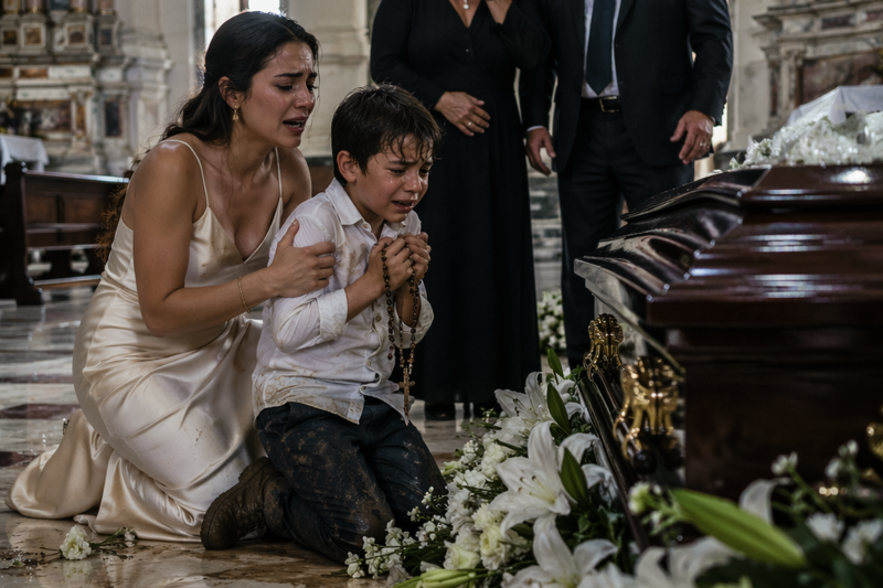 Em plena missa da minha avó, meu sobrinho voltou com os sapatos cheios de lama e sussurrou: “Ela não está sozinha.” Meu tio tentou calá-lo diante de 40 pessoas, mas minha mãe se levantou, apontou para o caixão e disse uma única frase… então ouvimos 3 batidas vindas da madeira fechada.